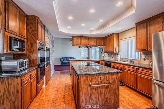 kitchen featuring a raised ceiling, a sink, black appliances, decorative backsplash, and a kitchen island