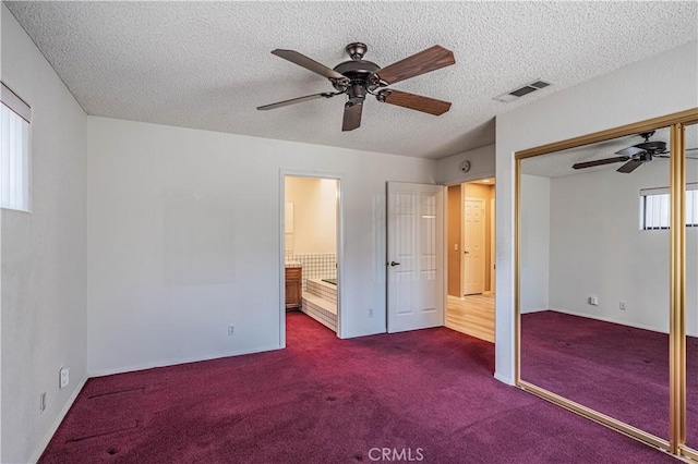 unfurnished bedroom with a closet, dark colored carpet, visible vents, and a textured ceiling