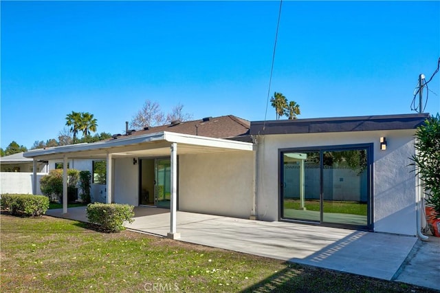 rear view of property with a patio area, a carport, stucco siding, and a yard