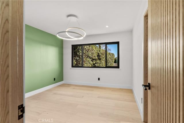 spare room with light wood-type flooring, baseboards, and a notable chandelier