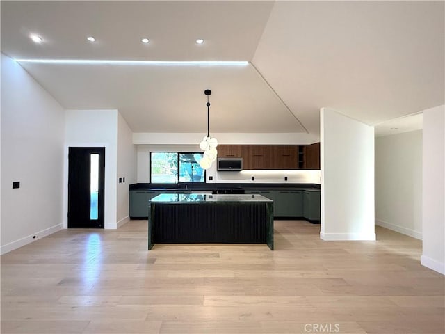 kitchen with a center island, stainless steel microwave, dark countertops, and light wood-type flooring