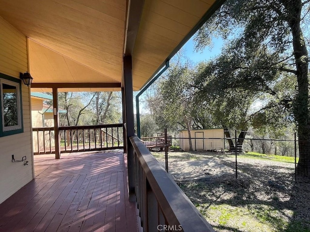 wooden deck featuring a storage unit, fence, and an outdoor structure