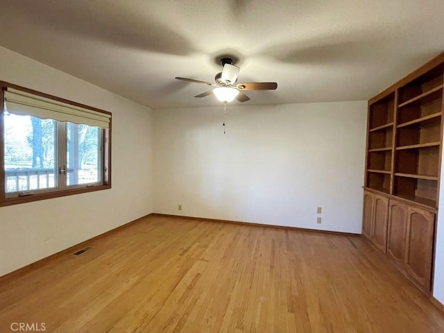 empty room with built in features, a ceiling fan, visible vents, light wood finished floors, and baseboards