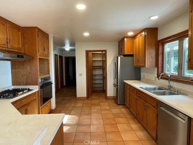 kitchen featuring a sink, light countertops, under cabinet range hood, brown cabinets, and stainless steel appliances