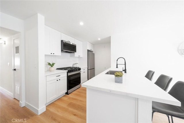 kitchen featuring stainless steel appliances, a kitchen breakfast bar, a sink, and white cabinetry