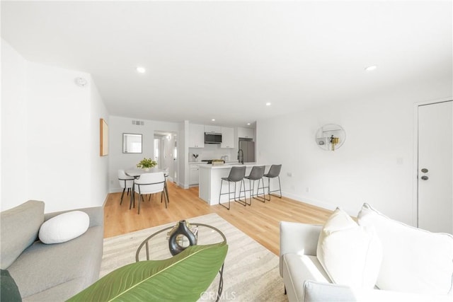 living room with visible vents, baseboards, light wood-type flooring, and recessed lighting