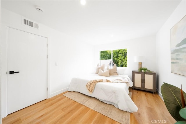 bedroom with light wood finished floors, visible vents, and baseboards
