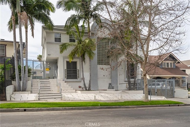 view of front of property featuring stucco siding, fence, and stairway