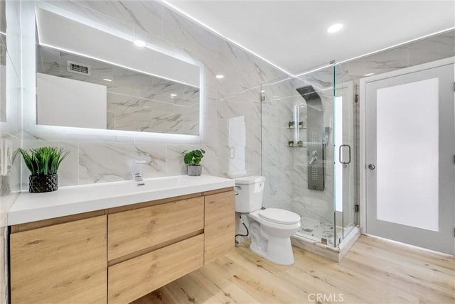 bathroom featuring a marble finish shower, toilet, visible vents, tile walls, and wood finished floors