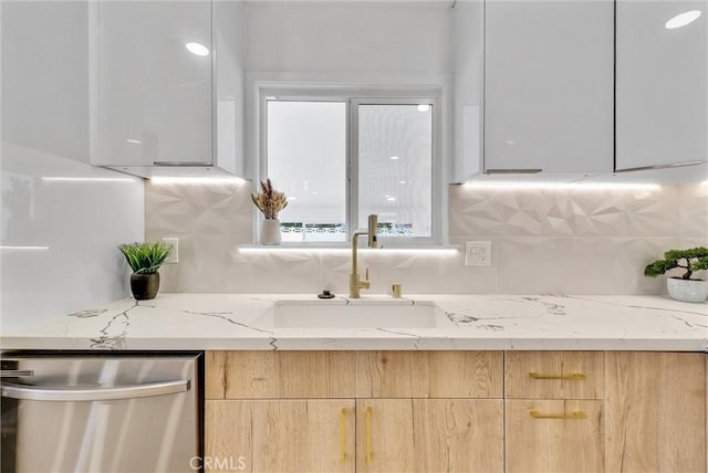 kitchen featuring stainless steel dishwasher, modern cabinets, light brown cabinets, and a sink