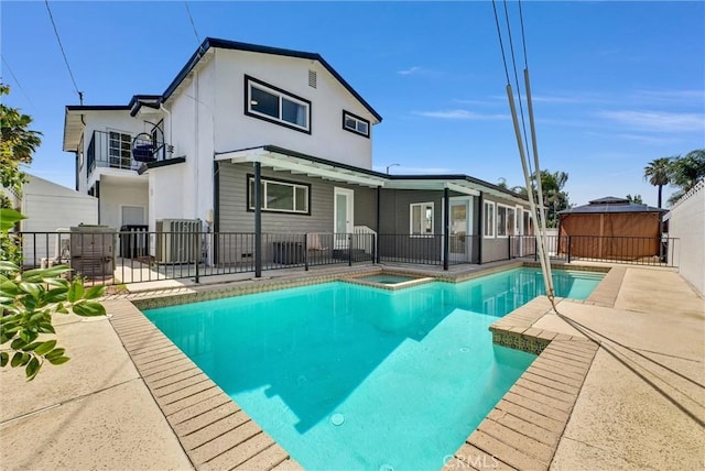 rear view of property featuring a fenced in pool, a patio, stucco siding, an outdoor hot tub, and fence