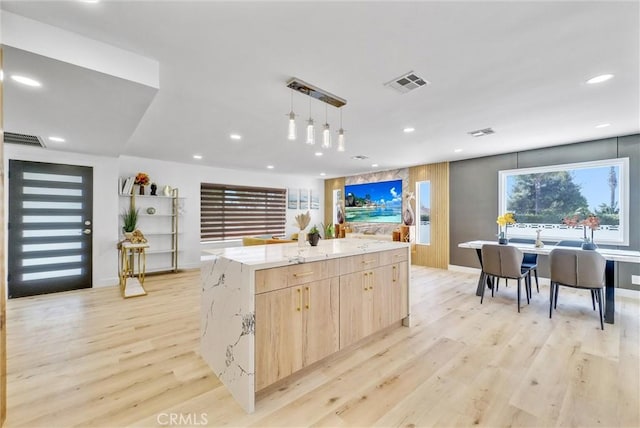 kitchen featuring light wood-type flooring, light stone counters, light brown cabinetry, and visible vents
