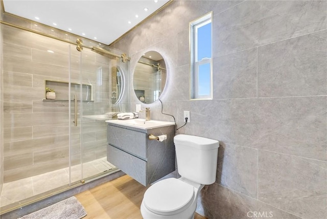 bathroom with tile walls, toilet, a stall shower, and vanity