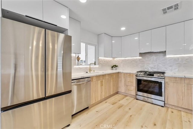 kitchen featuring visible vents, appliances with stainless steel finishes, light brown cabinetry, and modern cabinets