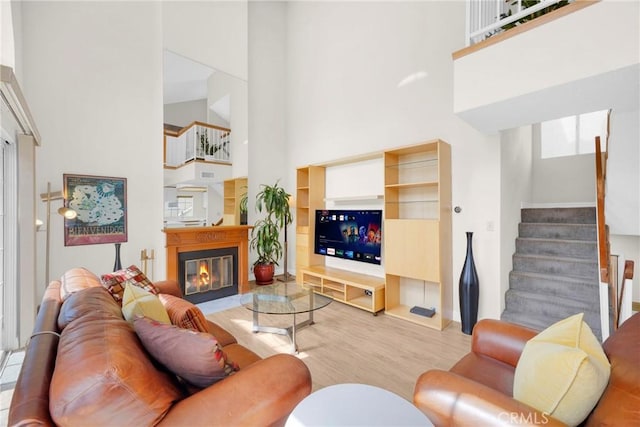 living area with wood finished floors, stairway, a glass covered fireplace, and a towering ceiling