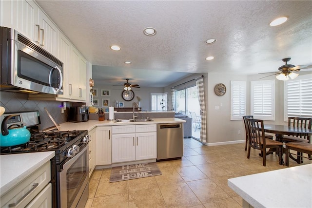 kitchen featuring ceiling fan, a peninsula, appliances with stainless steel finishes, light countertops, and a sink