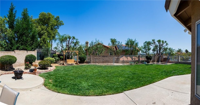 view of yard featuring a patio area, a fenced backyard, a playground, and an outdoor fire pit