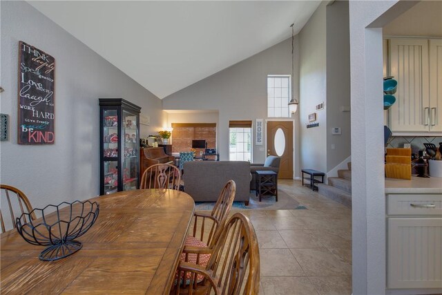 dining room featuring high vaulted ceiling, light tile patterned floors, and stairs