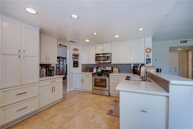 kitchen with a peninsula, visible vents, a sink, stainless steel appliances, and decorative backsplash
