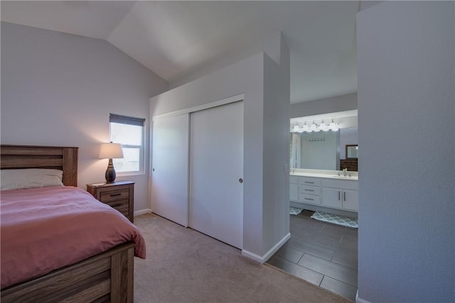 carpeted bedroom with a closet, ensuite bath, a sink, lofted ceiling, and tile patterned floors