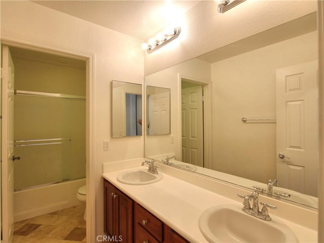 full bathroom featuring a sink, toilet, double vanity, and shower / bath combination with glass door