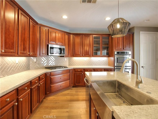kitchen with tasteful backsplash, light wood-style floors, appliances with stainless steel finishes, a sink, and hanging light fixtures