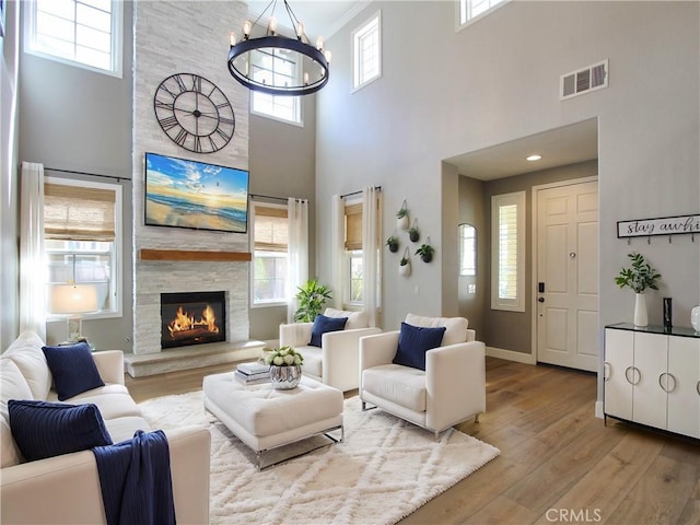 living area featuring an inviting chandelier, a stone fireplace, visible vents, wood finished floors, and baseboards