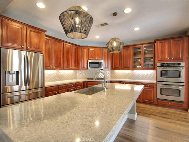 kitchen with visible vents, a sink, light wood-type flooring, light stone countertops, and stainless steel appliances