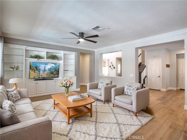 living area with ornamental molding, stairway, light wood-style flooring, a ceiling fan, and visible vents