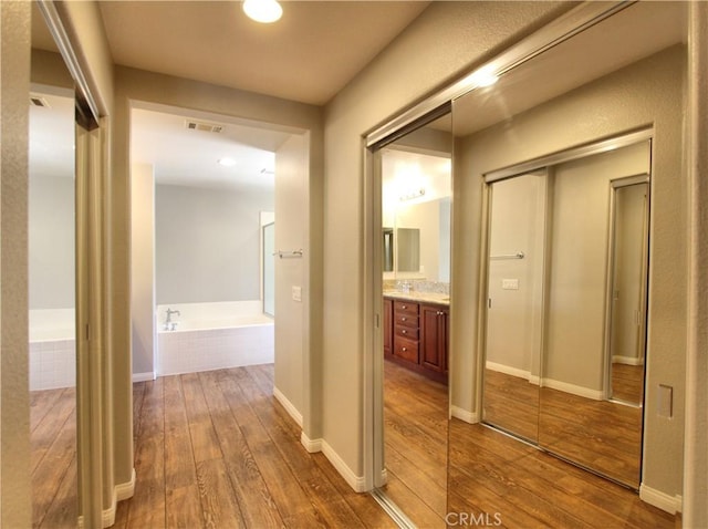 corridor featuring wood-type flooring, visible vents, and baseboards