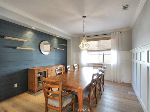 dining room with light wood finished floors, ornamental molding, and visible vents