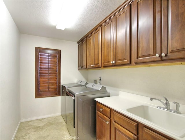 washroom featuring independent washer and dryer, a textured ceiling, a sink, baseboards, and cabinet space