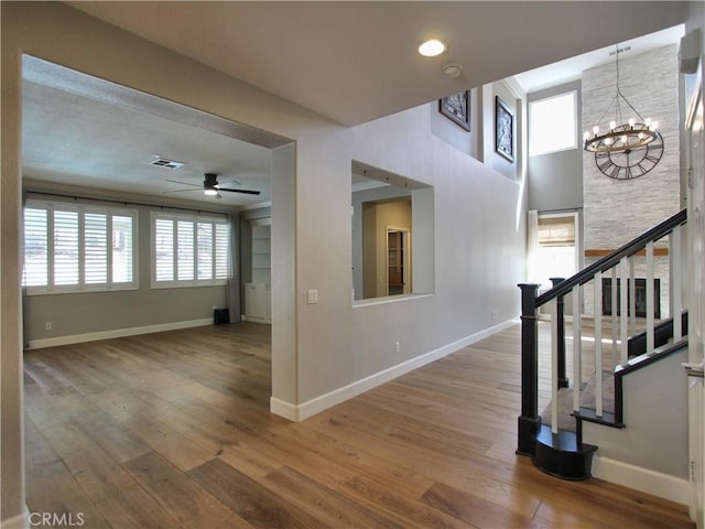 interior space featuring ceiling fan with notable chandelier, visible vents, stairway, wood finished floors, and baseboards