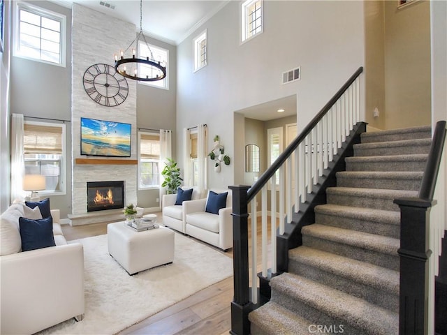living room featuring crown molding, visible vents, stairway, a chandelier, and wood finished floors