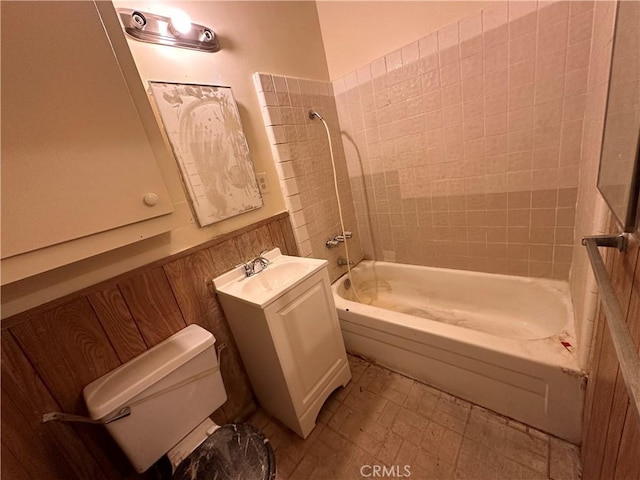 bathroom featuring toilet, vanity, shower / bathing tub combination, and a wainscoted wall