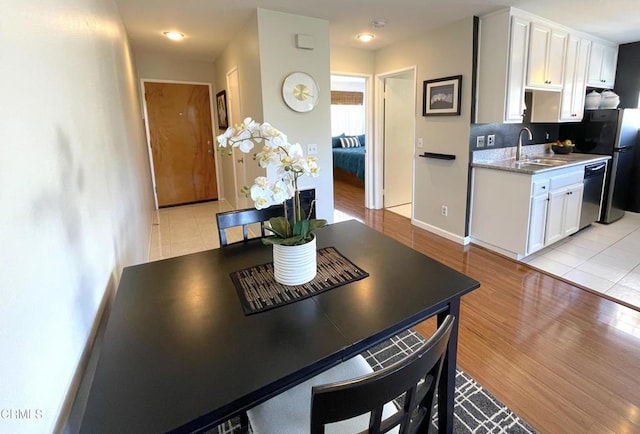 kitchen with light countertops, white cabinets, light wood-style floors, dishwashing machine, and a sink