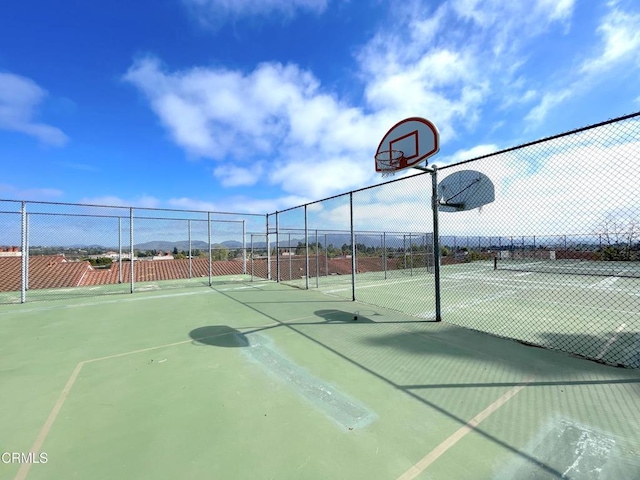 view of tennis court featuring community basketball court and fence