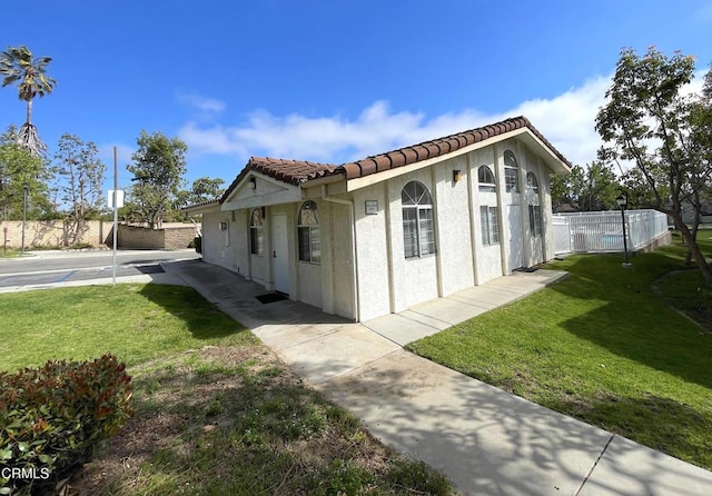 view of property exterior with a yard, stucco siding, fence, and a tile roof