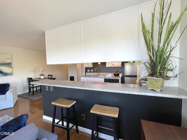 kitchen featuring freestanding refrigerator, a peninsula, a breakfast bar, a sink, and dark wood-style floors