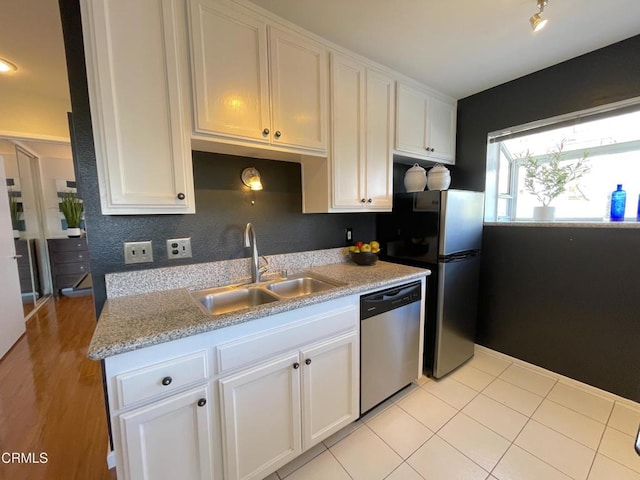 kitchen featuring appliances with stainless steel finishes, light tile patterned flooring, a sink, and white cabinets