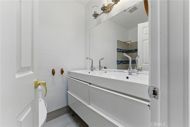 bathroom featuring vanity, visible vents, a tile shower, and toilet