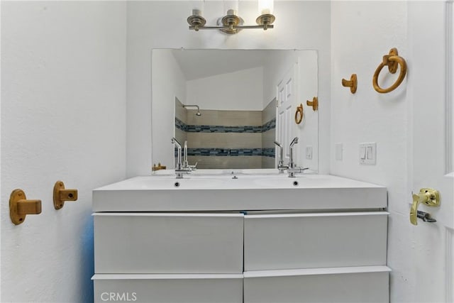 full bathroom with a sink, tiled shower, and double vanity