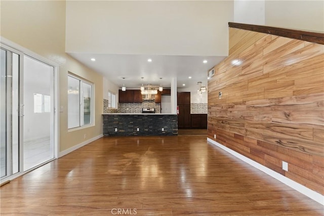 unfurnished living room with a towering ceiling, a chandelier, wood walls, visible vents, and wood finished floors