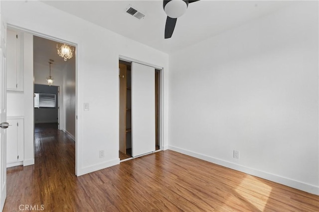 unfurnished bedroom featuring ceiling fan with notable chandelier, a closet, visible vents, wood finished floors, and baseboards