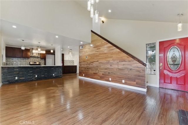 foyer entrance with visible vents, baseboards, wood finished floors, wood walls, and high vaulted ceiling