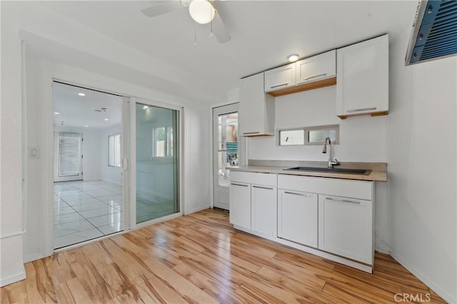 kitchen featuring light wood-type flooring, light countertops, white cabinetry, ceiling fan, and a sink
