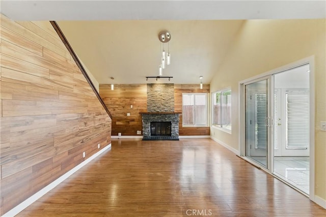 unfurnished living room with a fireplace, vaulted ceiling, wood finished floors, wood walls, and rail lighting