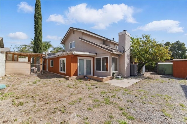 rear view of house featuring central air condition unit, stucco siding, a chimney, french doors, and fence