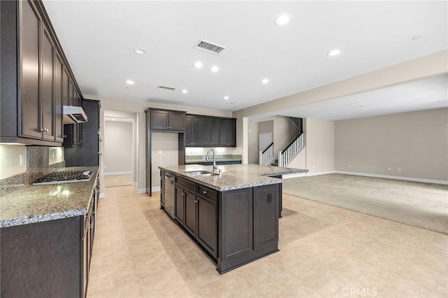 kitchen featuring dark brown cabinets, under cabinet range hood, a sink, and light stone counters