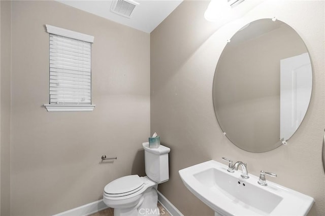 half bath with visible vents, toilet, baseboards, and a sink